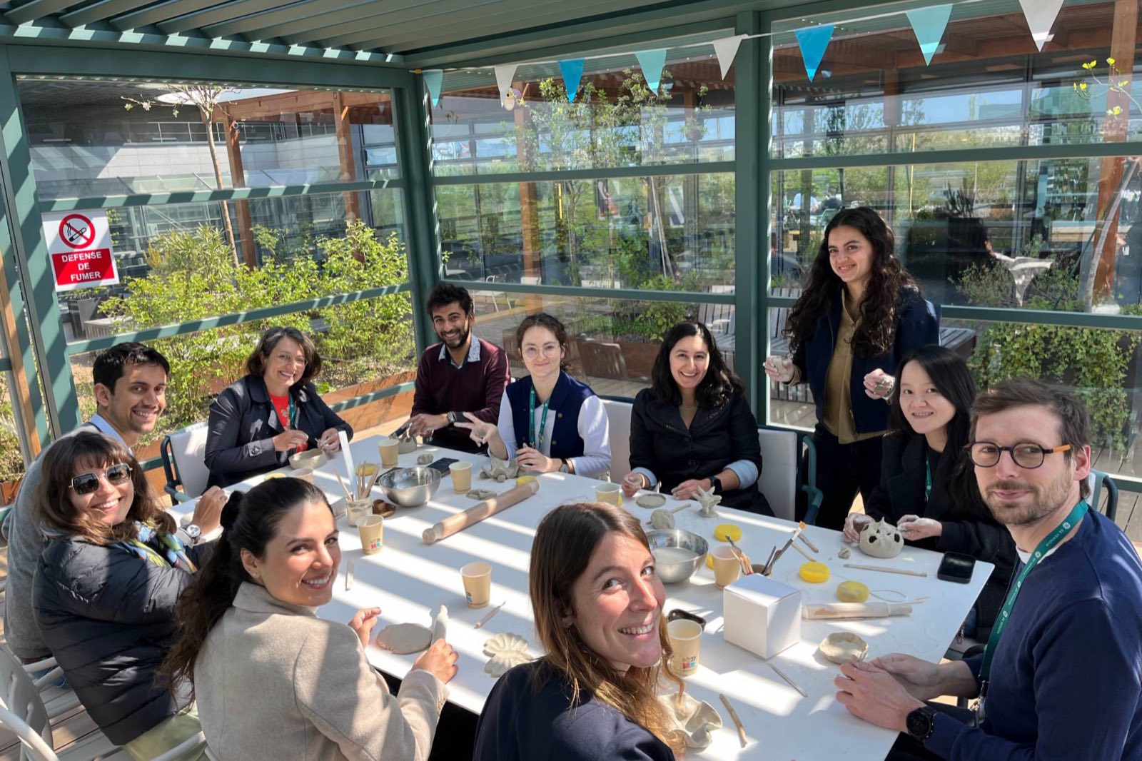 Atelier poterie en entreprise : Marie D’Antoni et des salariés souriants autour d’une grande table, sur une terrasse